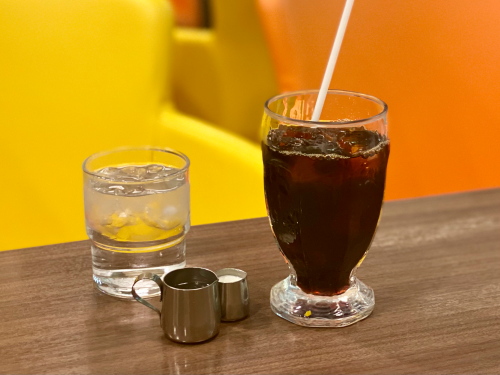 ロゴ入りのグラスに注がれたアイスコーヒーと別添えのシロップ
