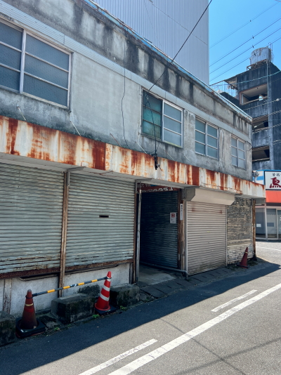 シャッターが閉じた古いコンクリートビルの1階中央にぽっかりと開いた薄暗い屋内通路の入り口