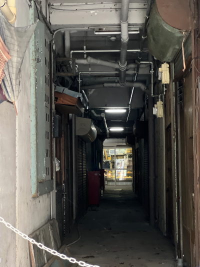 配線や配管が天井にむき出しになり、薄暗いビルの中に店舗の扉が並ぶレトロな内部通路