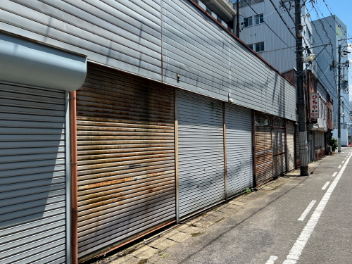 無機質なグレーのシャッターが並ぶ通りで、ひっそりと営業を続けるひちやの店舗外観