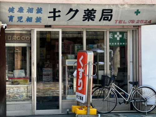 キク薬局の健康相談と書かれた古い看板と角に併設された小さなたばこ売店の窓口