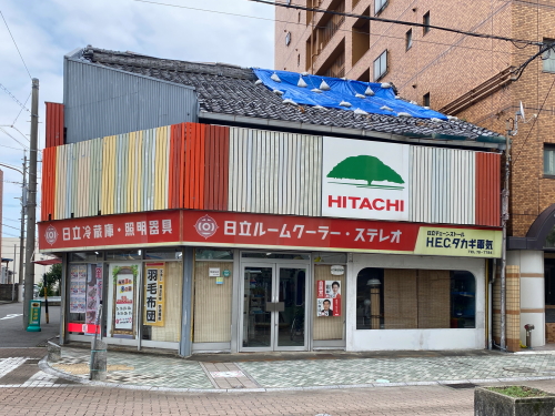 日立の木ロゴマークと大きな曲線窓が特徴的な古い街の電器店のファサード