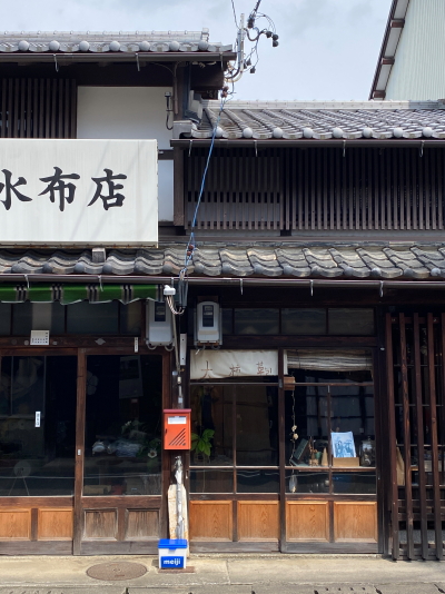 使い込まれた木製枠の引き戸ガラスと、素朴な佇まいを見せる岡田防水布店の入り口の軒先