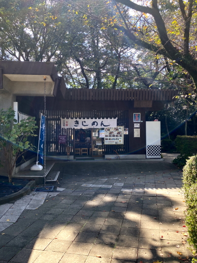 豊かな樹木に囲まれた、落ち着きのある和風建築の名古屋城きしめん亭の外観。入り口には大きく「きしめん」と書かれたのれんが掛かっており、右手には大きなメニュー看板が設置されています。