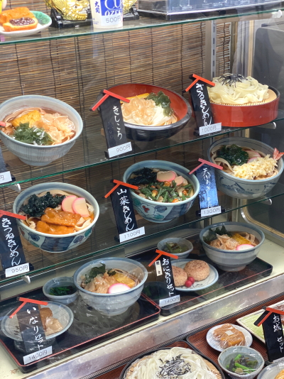 名古屋城きしめん亭の店外に設置された、様々なきしめんやサイドメニュー、お弁当の食品サンプルが並ぶショーケース。海外からの観光客にも視覚的にメニューが分かりやすい配置です。