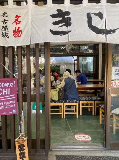 木の温もりを感じる和風デザインの名古屋城きしめん亭の店内。等間隔に配置されたテーブル席に観光客が座って食事をしており、落ち着いた庶民的で活気のある雰囲気が漂っています。