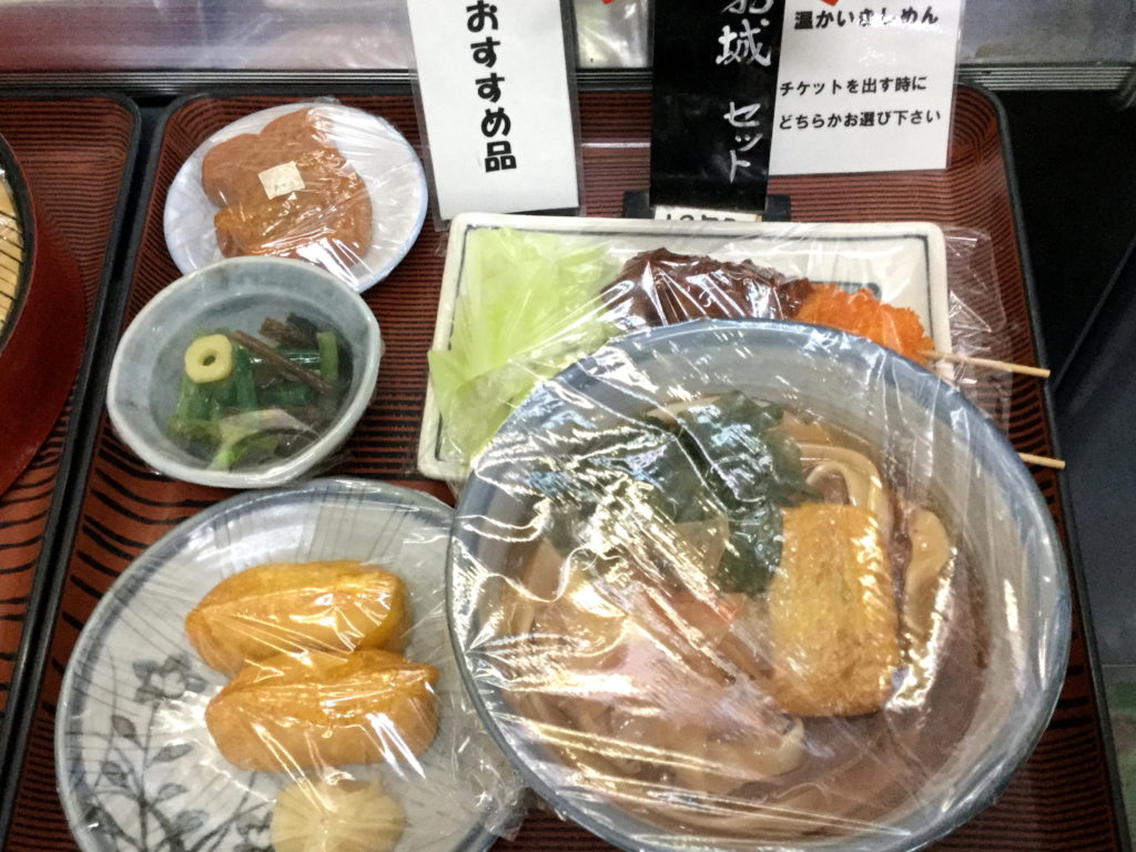 お盆に載ったボリュームたっぷりの名古屋城セット（1,600円）。かつお節の載った温かいきしめん、いなり寿司2個、ソースのたっぷりかかった味噌串カツ2本、お城デザインの甘味「金シャチ焼」が1つのセットになっています。